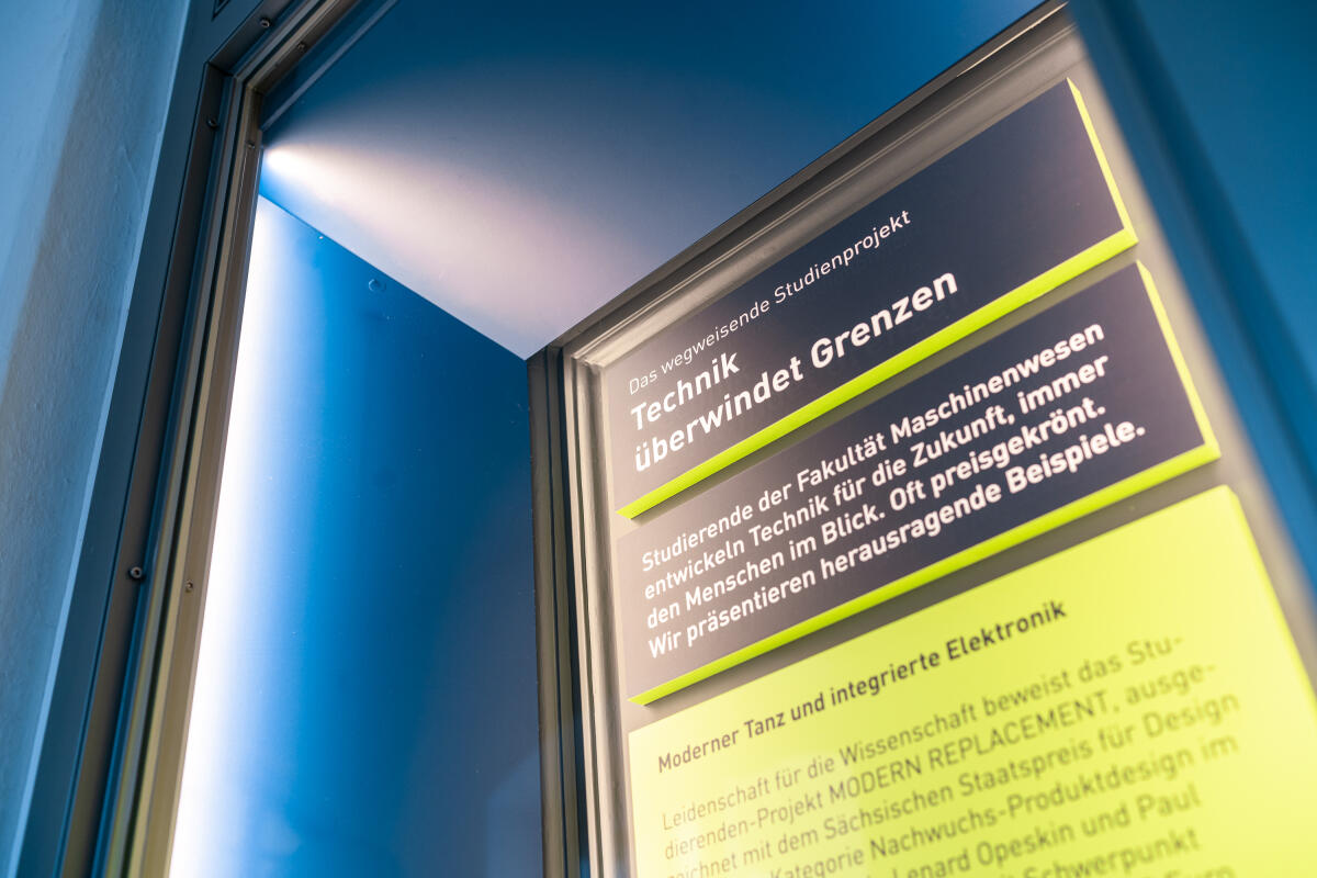 Ein interaktives Ausstellungsplakat, das Informationen über ein Studienprojekt zur Technik bietet, das Grenzen überwindet. Das Plakat enthält helle Schriftzüge auf einem kontrastreichen Hintergrund, der die Bedeutung von Maschinen und Technik für die Zukunft betont. Im Hintergrund ist eine Lichtquelle zu sehen, die eine positive Atmosphäre schafft.