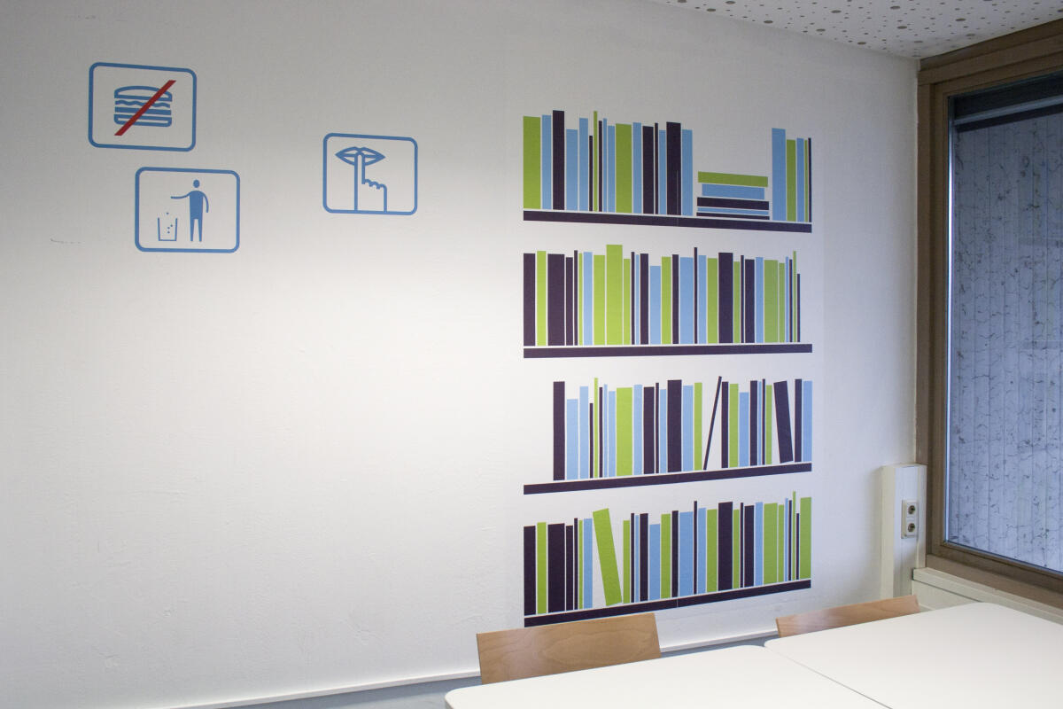 An einer Wand sind symmetrische Regale mit bunten Bücher-Illustrationen in verschiedenen Höhen und Breiten dargestellt. Daneben sind drei einfache Piktogramme, die ein Verbotsschild, eine Person und ein Telefon zeigen. Dieser Raum hat große Fenster, die Licht hereinlassen.
